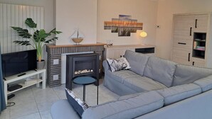 Ein Wohnzimmer mit grauem Sofa, Fernseher, Kamin und Bücherregal.