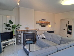 A living room with a grey sofa, a TV, a fireplace, and a bookshelf. - Bright Apartment With Side Sea View (Koksijde)