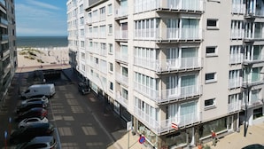 Ein mehrstöckiges Hotel mit Balkonen, Blick auf den Strand und einem Parkplatz mit Autos.