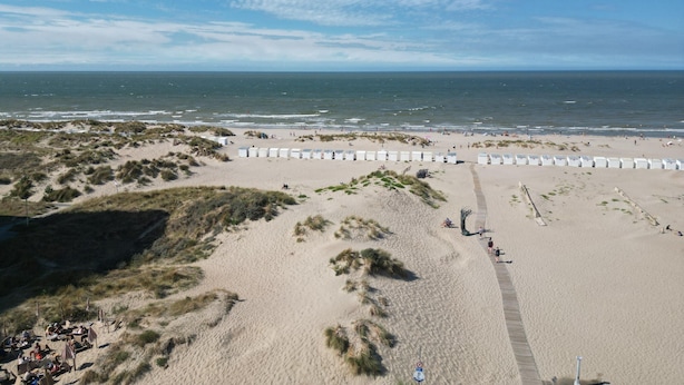 Ein Strand mit Dünen, einem Holzsteg und Strandkörben.