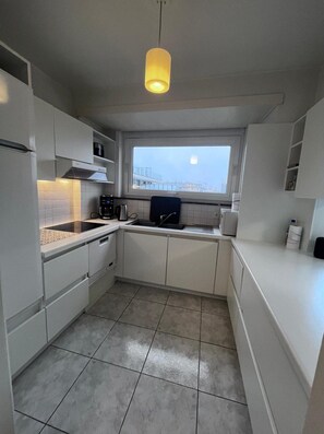 A compact kitchen with white cabinetry, a built-in oven, and a window above the sink. - Bright Apartment With Side Sea View (Koksijde)