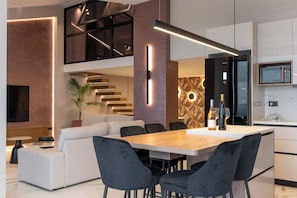 A modern kitchen with a built-in microwave, a dining area with a wooden table and black chairs, and a living area with a sofa and a TV. - Pnoi Sea View Villas Piskopiano (Piskopiano)