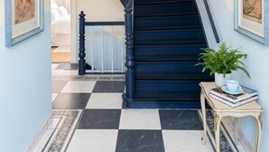 Eine prächtige Treppe mit Schachbrettfußboden in Schwarz und Weiß, einem Kronleuchter und gerahmten Kunstwerken an den Wänden.