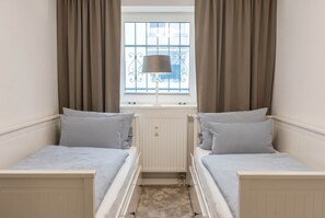 A bedroom with two beds, a window with curtains, a radiator, and a lamp.
