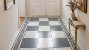 Um corredor com piso xadrez, portas duplas com painéis de vidro, um lustre e um espelho grande na parede.