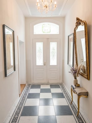 A hallway with a checkered floor, double doors with glass panels, a chandelier, and a large mirror on the wall. - Captain's apartment Villa Kaethe Kurpark (Rostock)
