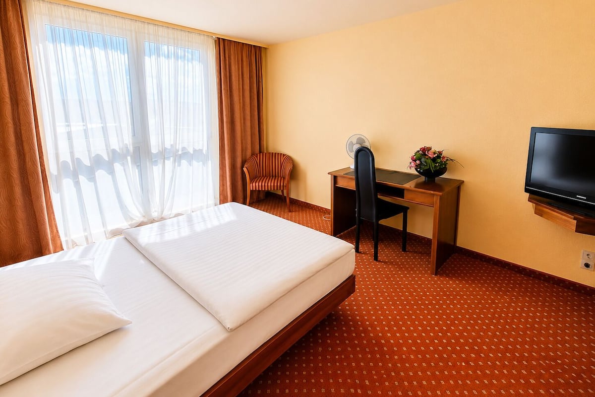 Ein Hotelzimmer mit einem Bett, einem Schreibtisch, einem Sessel, einem Fernseher und einem großen Fenster mit Vorhängen.