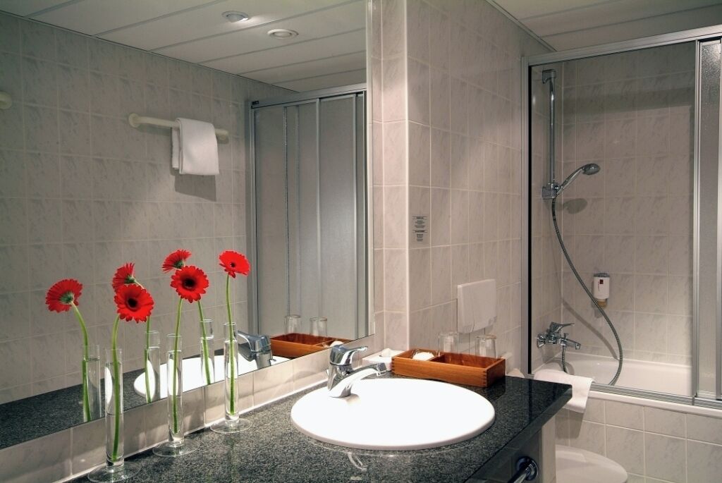Un baño con un espejo grande, un lavabo, una ducha y un perchero para toallas.