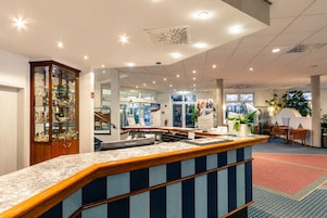A reception area with a marble counter, a wooden display cabinet, and a seating area with chairs and a table.