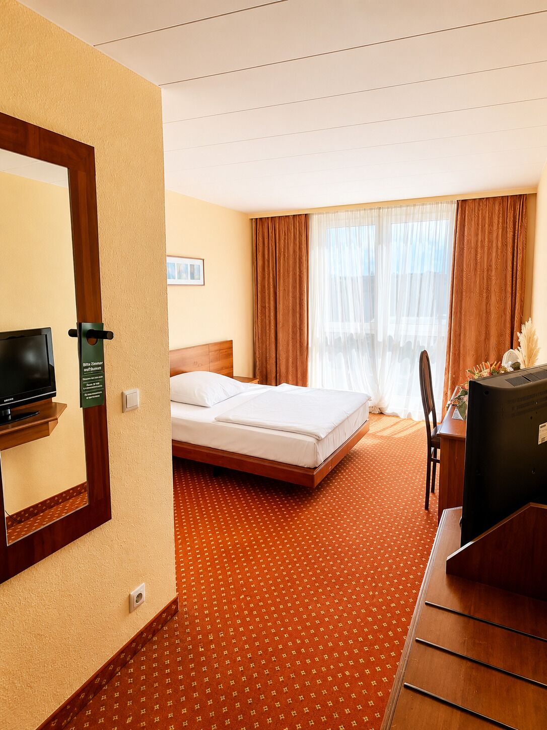 A hotel room with a bed, a television, a desk, and a window with curtains.