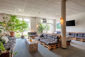 A modern lounge area with cushioned seating, potted plants, and a large pillar. - Quick Hotel Dresden 24H Self Check-in (Wilsdruff)