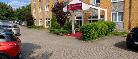 A Quick Hotel Dresden West with a brick facade, multiple windows, and a parking area with cars.