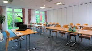 Een vergaderruimte met tafels, stoelen, een laptop, een beamer en een raam met uitzicht op groen.