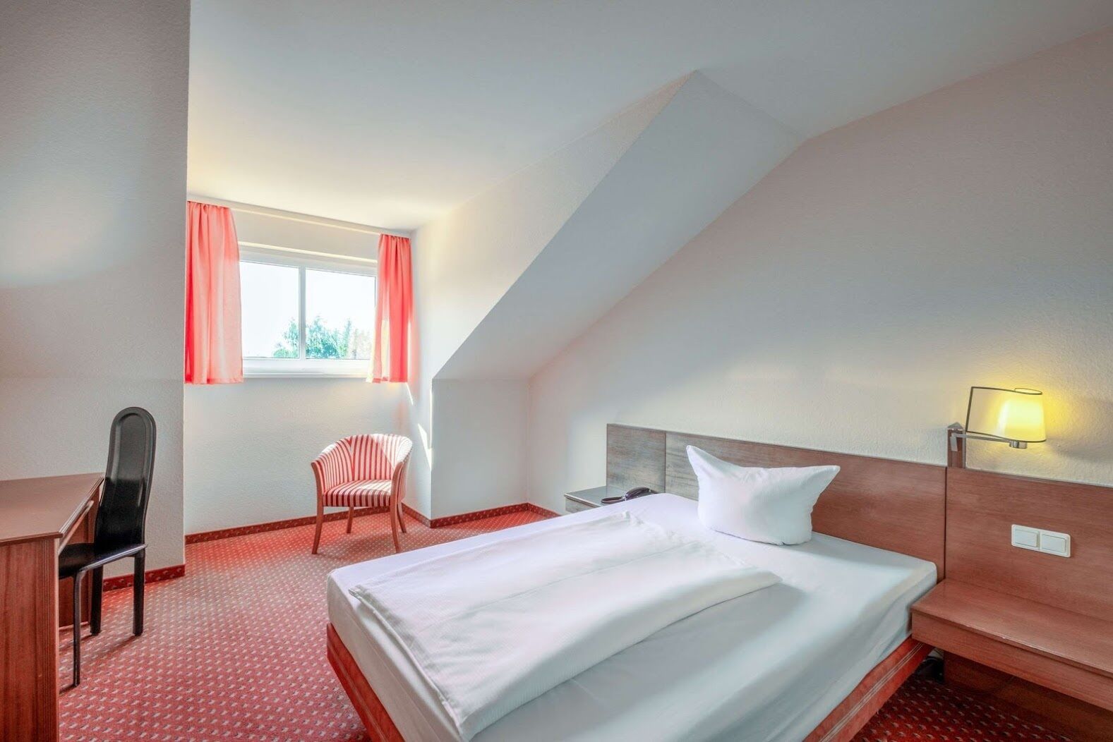 A hotel room with a bed, desk, chair, and a window with curtains.