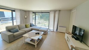 En moderne stue med en modulsofa, et sofabord, et fjernsyn og store vinduer med gardiner.