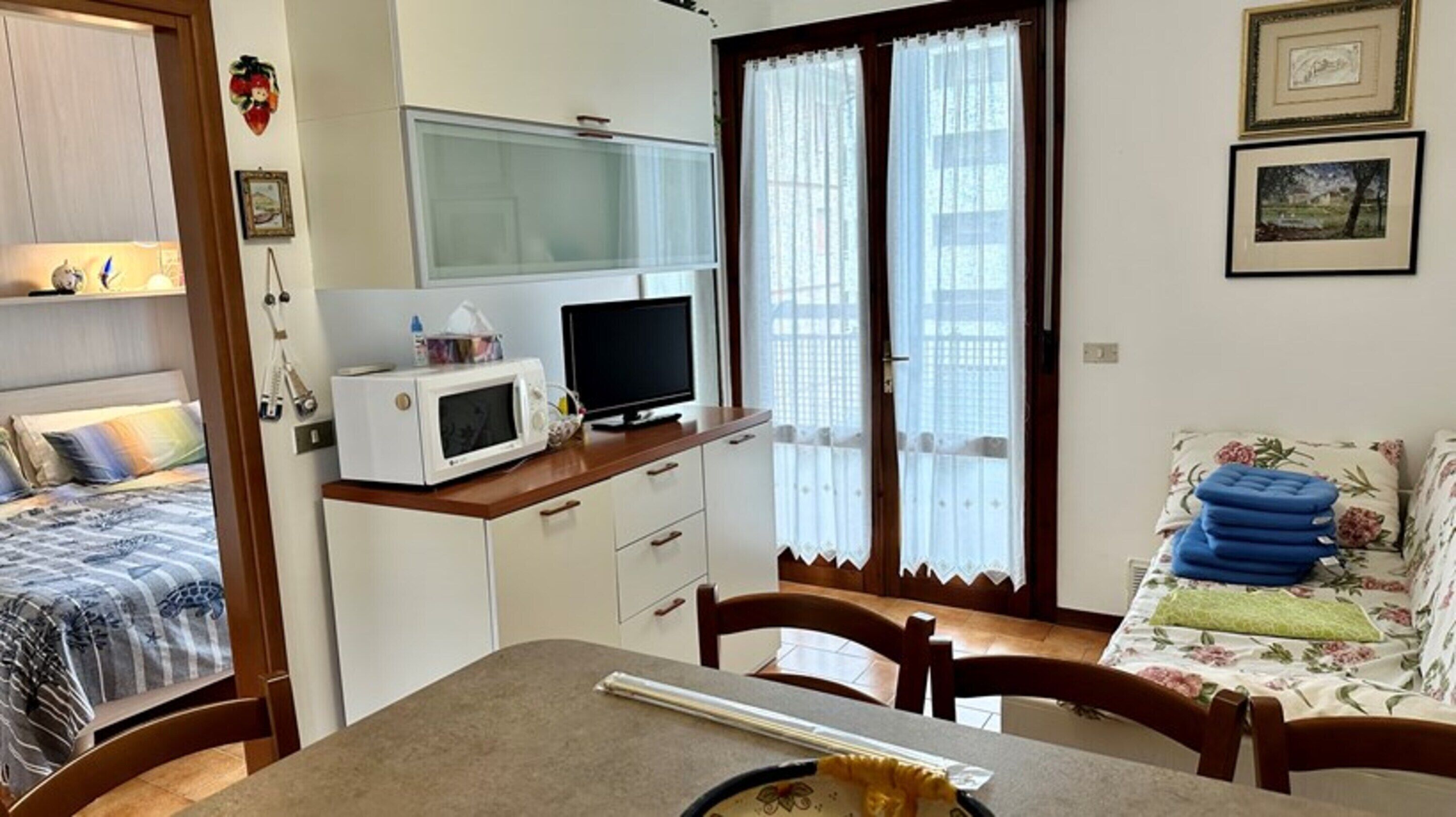 Une pièce de taille modeste comprenant un lit, une table à manger, un four à micro-ondes, un téléviseur et une fenêtre avec des rideaux.