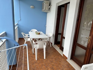 Ein Balkon mit weißem Tisch und Stühlen, einer blauen Wand und einer Schiebeglastür.