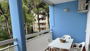 Ein Balkon mit einem weißen Tisch und Stühlen, einer Obstkorb und Blick auf Bäume und Gebäude.