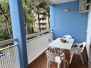 A balcony with a white table and chairs, a basket of fruit, and a view of trees and buildings. - Beachside Retreat for Families With Parking (San Michele al Tagliamento)