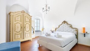 Een slaapkamer met een grote garderobe, een bed met wit beddengoed, een kroonluchter en een klein plankje met een kaars.