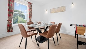 A dining area with a round table, six chairs, and a foosball table.