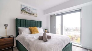 A bedroom with a bed, a nightstand, a window, and a painting on the wall.