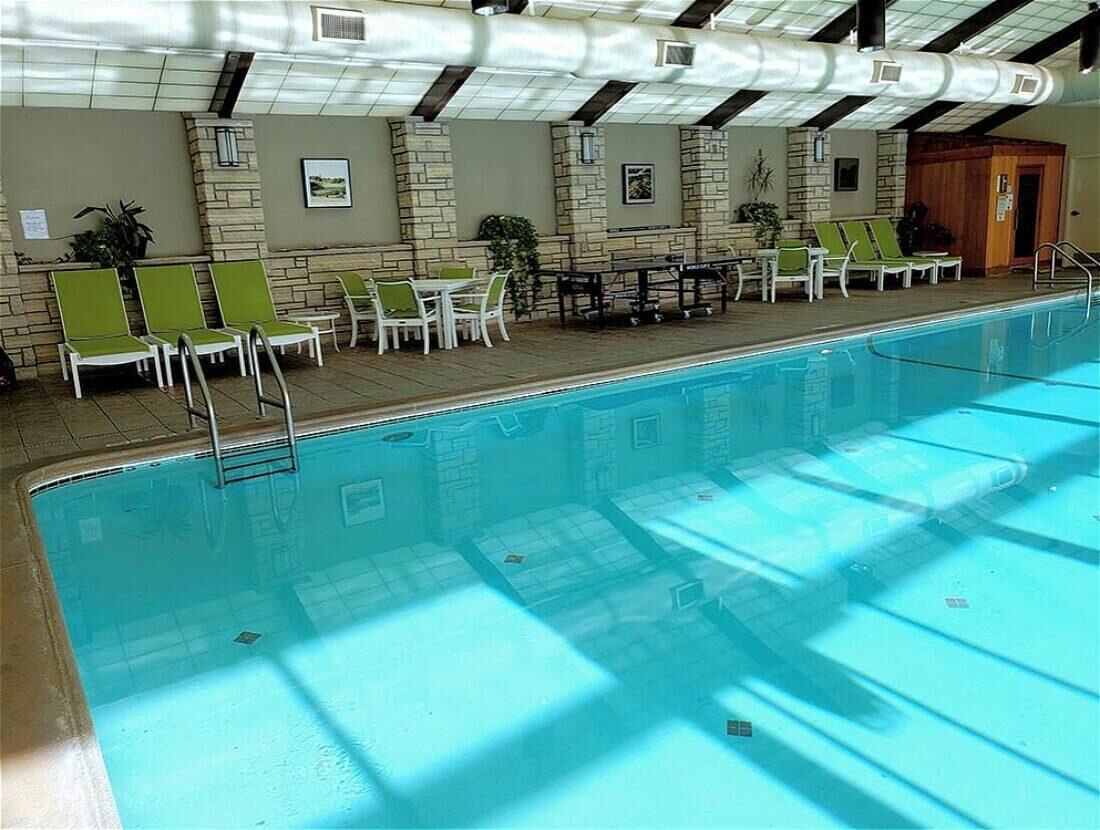 Ein Hallenbad mit Liegestühlen und Tischen, Steinwänden und einer Holztür.
