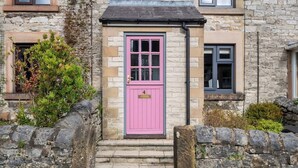 Un bâtiment en pierre avec une porte rose, un petit porche et un mur en pierre.