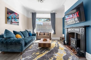 A living room with a sofa, a coffee table, a fireplace, and a TV mounted on the wall.