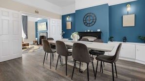 Un coin repas avec une longue table, six chaises, une horloge au mur et une cheminée.