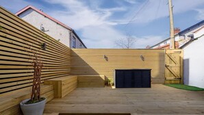 Une terrasse en bois avec un banc, un pot de fleurs et une porte de garage.