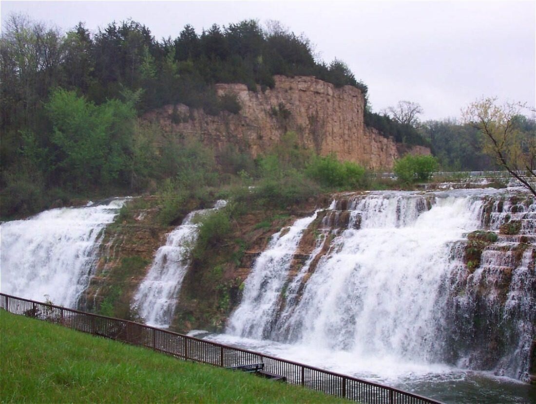 A waterfall cascading over a rocky cliff with a metal railing in the foreground.