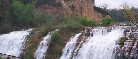 A waterfall cascading over a rocky cliff with a metal railing in the foreground.