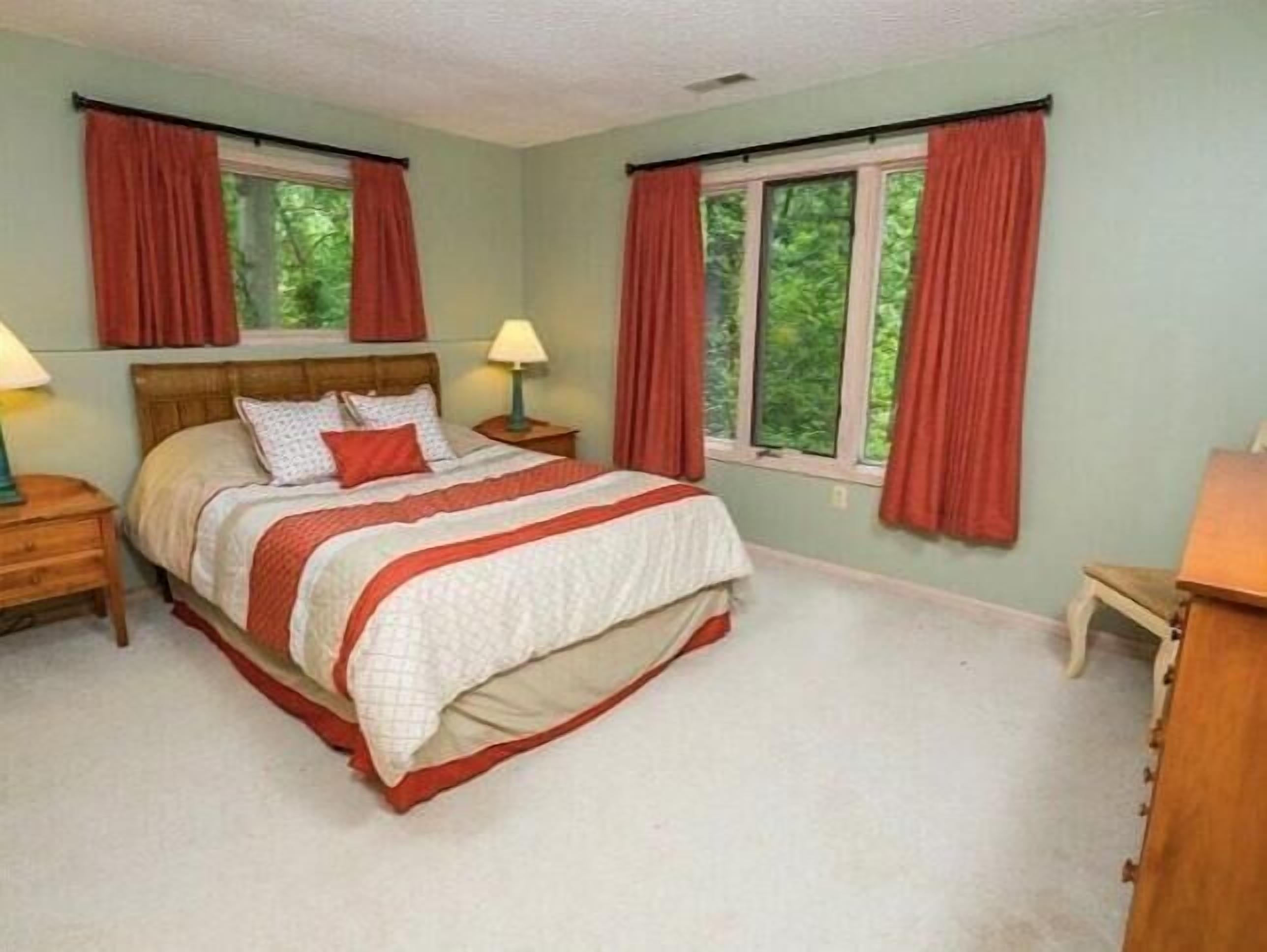 Ein Schlafzimmer mit einem Bett, zwei Nachttischen, einer Kommode und zwei Fenstern mit Vorhängen.