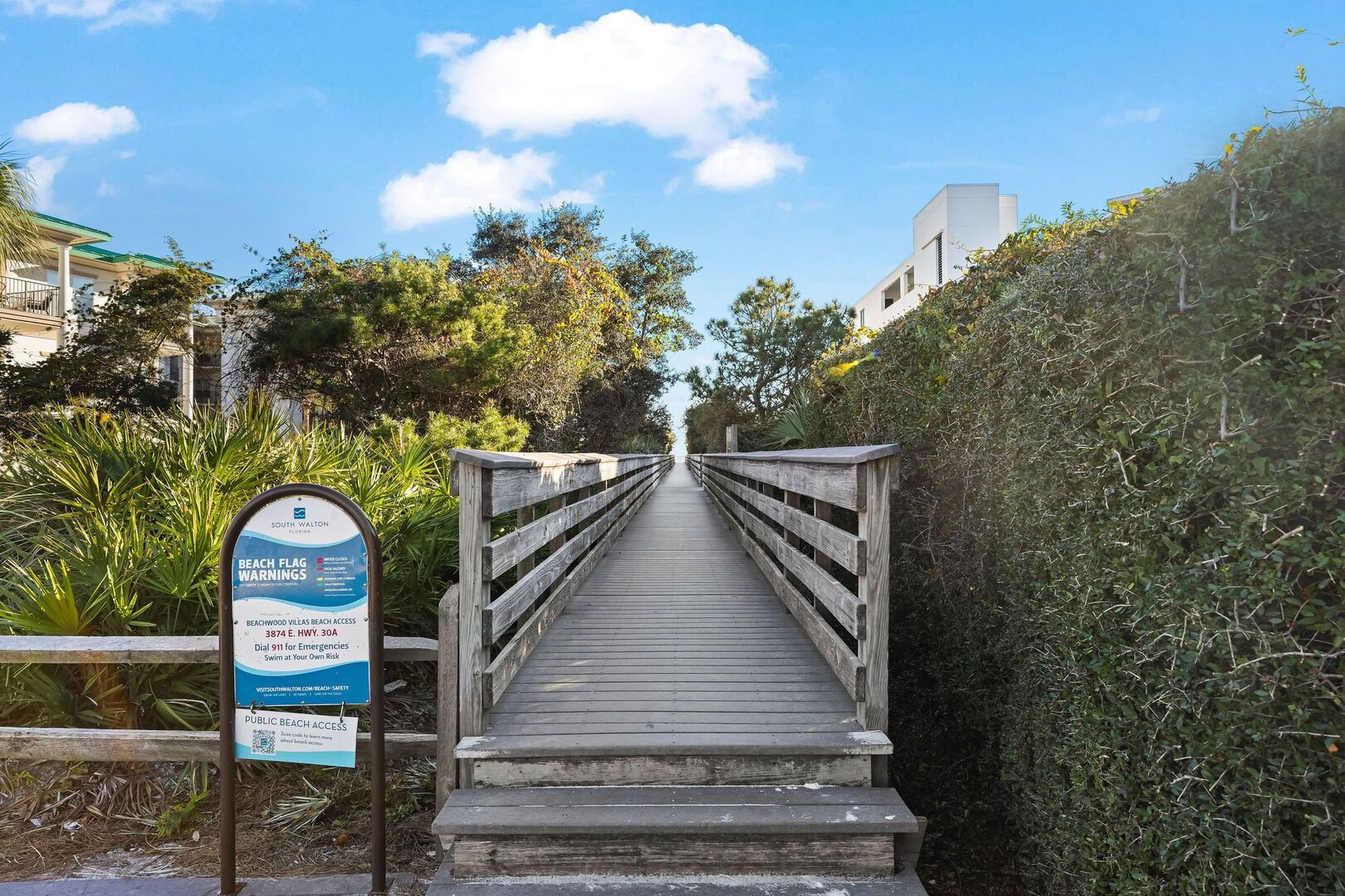 A wooden boardwalk leading to a beach area with a signboard providing beach access information.