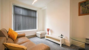 A living room with a brown leather sofa, a white ottoman, a glass coffee table, and a white side table with a vase and a lantern. - Stylish Modern Getaway : Lancashire (Lancashire)