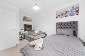 A bedroom with two beds, a bedside table, a lamp, and a painting on the wall.