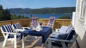 A deck with white chairs and a table, overlooking a lake with mountains in the background. - Serene Fjord View Holiday House in Davik, Nordfjord (Bremanger)