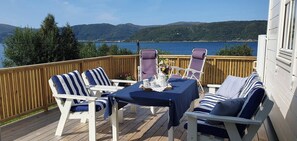 A deck with white chairs and a table, overlooking a lake with mountains in the background. - Serene Fjord View Holiday House in Davik, Nordfjord (Bremanger)