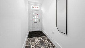 Un corridoio con pavimento decorato, una porta bianca con finestra e uno specchio fissato alla parete.