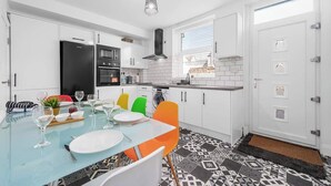 Una cucina moderna con mobili bianchi, un frigorifero nero e un tavolo da pranzo apparecchiato con piatti e bicchieri.