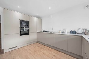 Una cocina moderna con electrodomésticos integrados, una encimera con hervidor y un ventilador de pared.