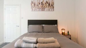 Een hotelkamer met een bed, een hoofdbord, een aan de muur hangend kunstwerk, een nachtkastje met een lamp en een deur.