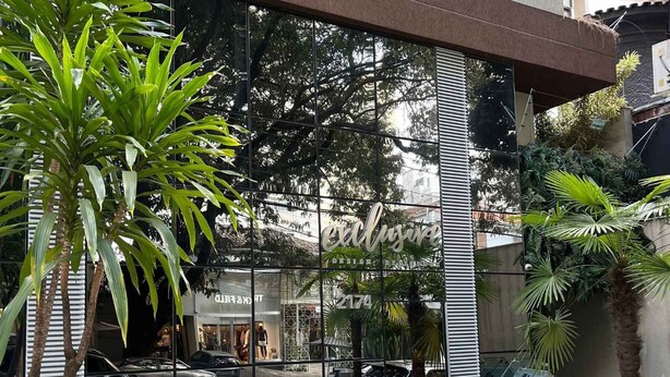 Un edificio moderno con una amplia fachada de vidrio, una piscina pequeña y abundante vegetación circundante.