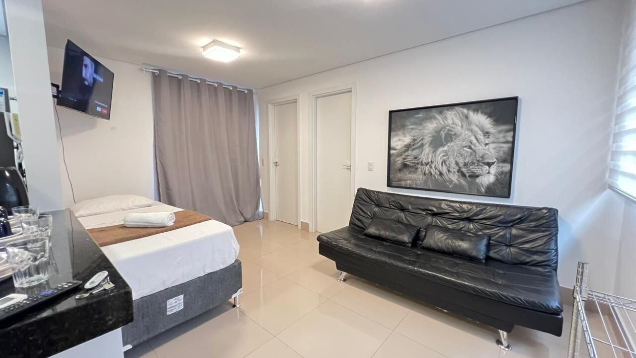 A hotel room with a bed, a black leather sofa, a mounted TV, and a framed picture on the wall.