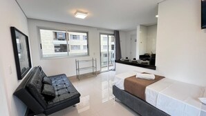 Habitación de hotel moderna con cama, sofá, una mesita, espejo y ventana con vistas a edificios.