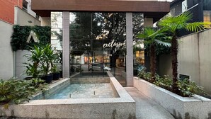 Un edificio moderno con fachada de vidrio, una piscina pequeña y plantas en macetas.