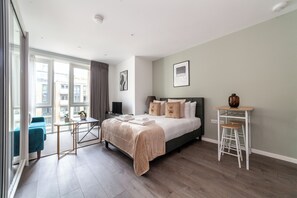 Ein modernes Schlafzimmer mit einem großen Bett, einem kleinen Tisch, einem Stuhl und einem Fenster mit Vorhängen.