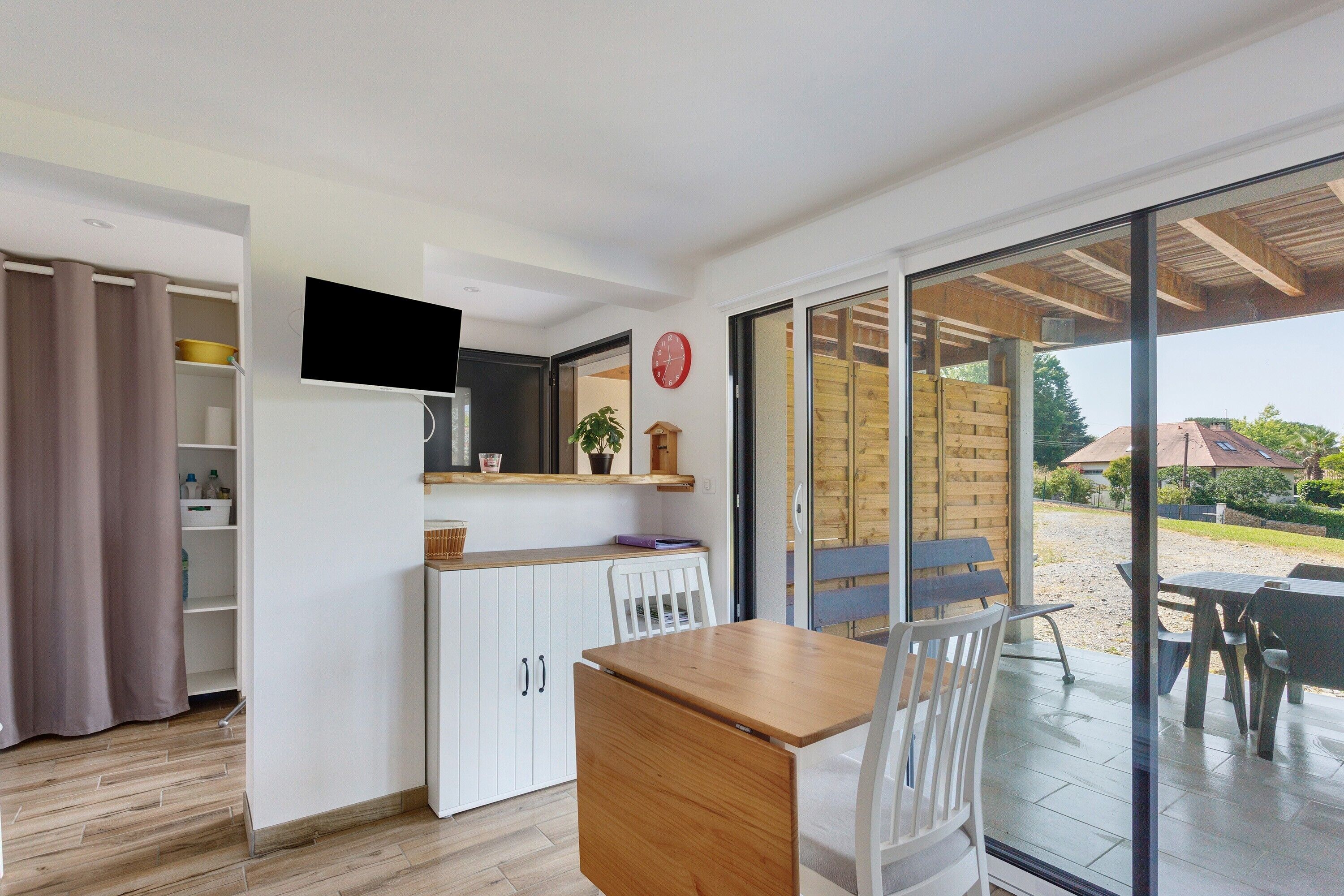 A modern kitchen with a built-in TV, a dining area with a table and chairs, and a sliding glass door leading to an outdoor patio.