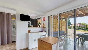 A modern kitchen with a built-in TV, a dining area with a table and chairs, and a sliding glass door leading to an outdoor patio.